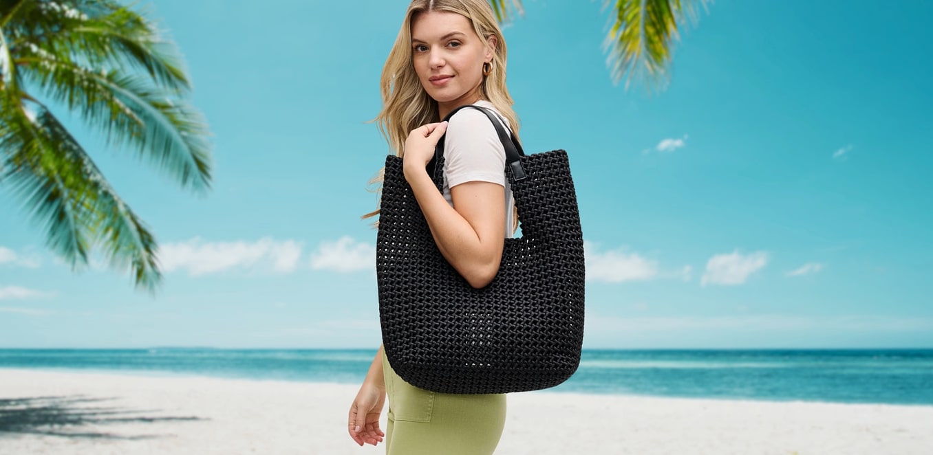 a model on a beach carrying a black woven tote bag