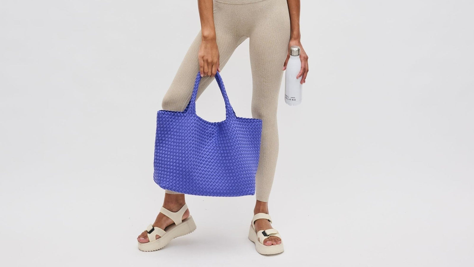 A woman in a beige yoga set holding a blue tote