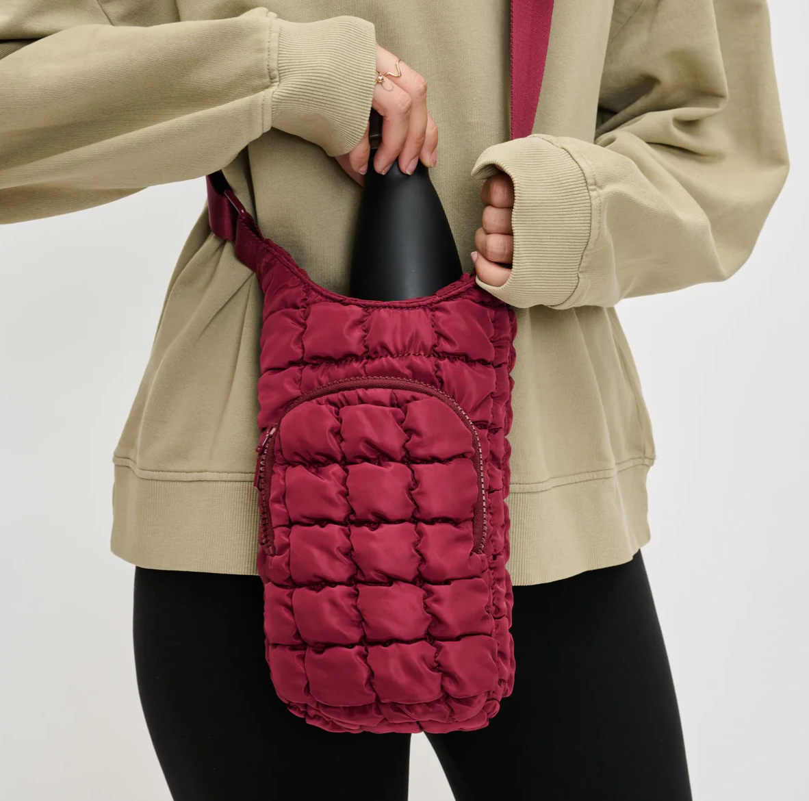model putting a water bottle into a burgundy puffer crossbody bag