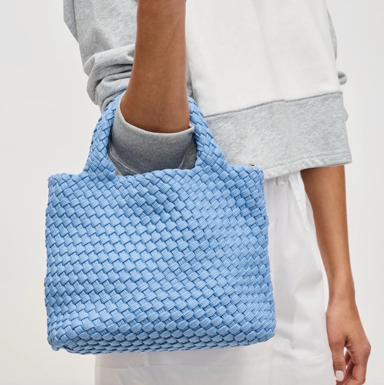 Person carrying a light blue woven handbag on their arm