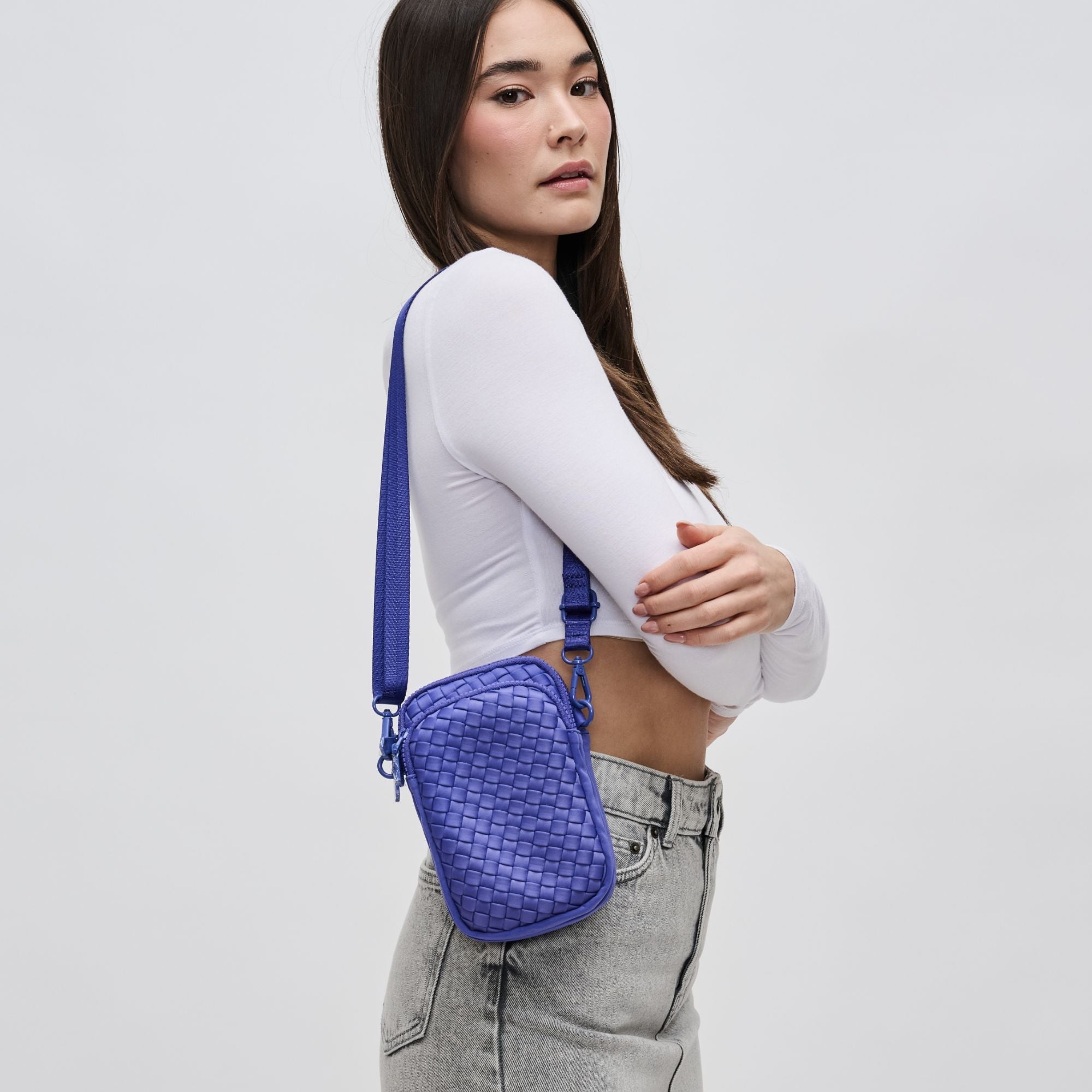 a model in a white top carrying a woven purple crossbody phone bag