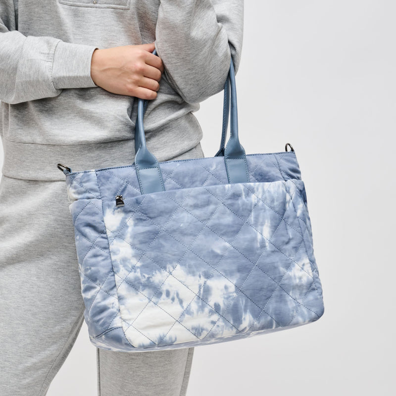 a model in gray holding a small blue and white tie-dye tote