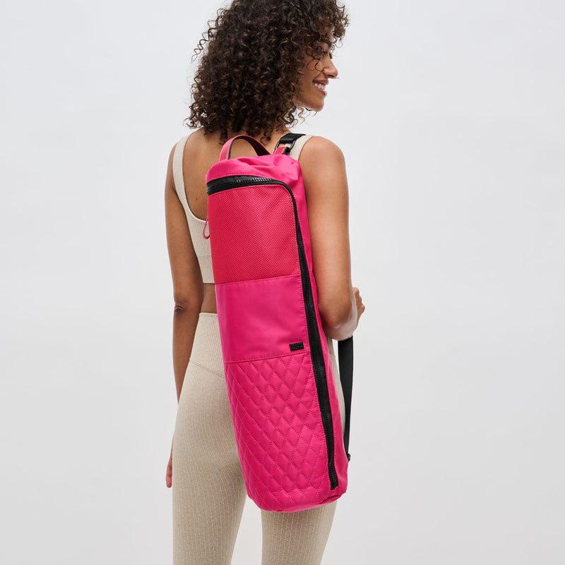 a model in activewear holding a bright pink yoga mat carrying bag