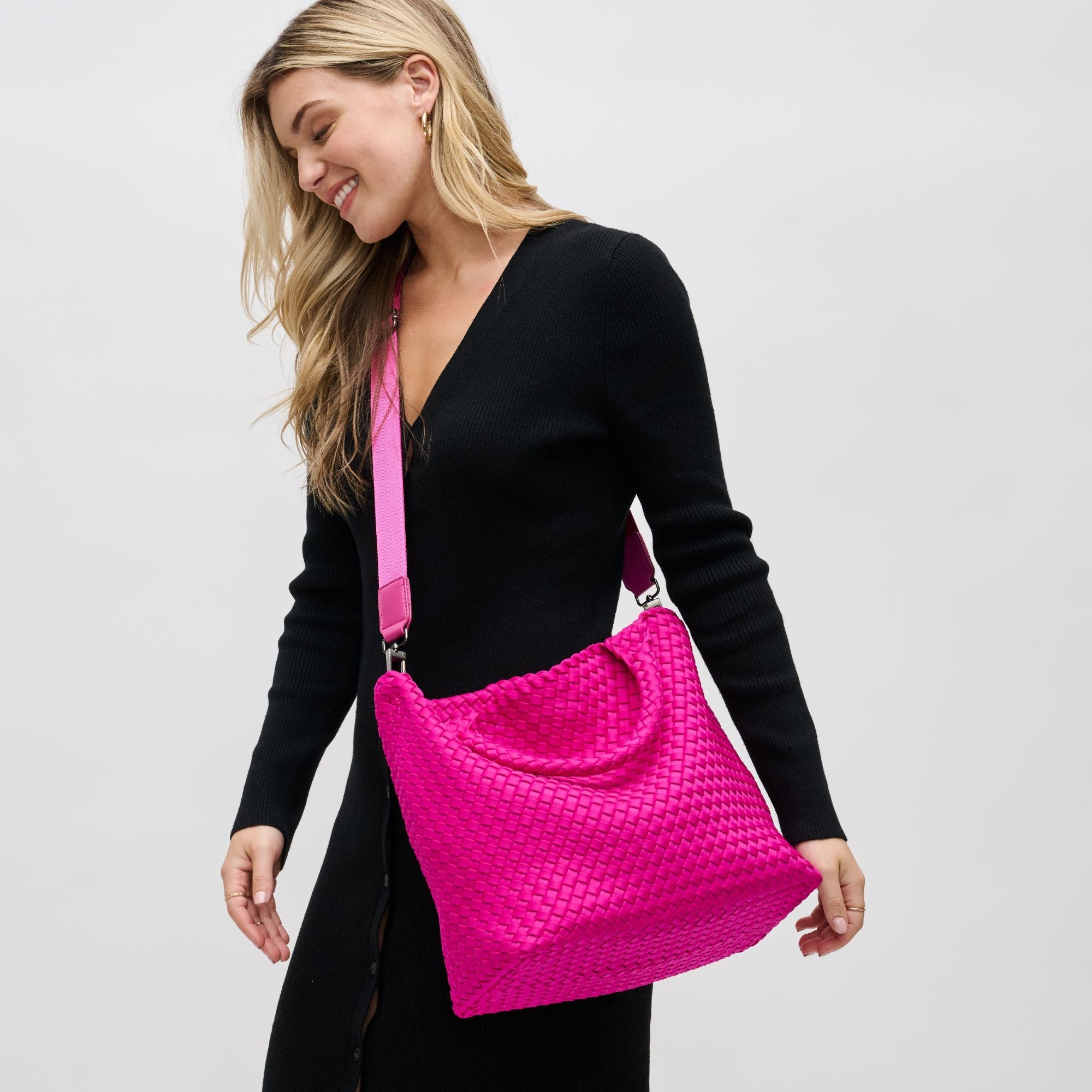 a model in black carrying a neon pink crossbody tote bag