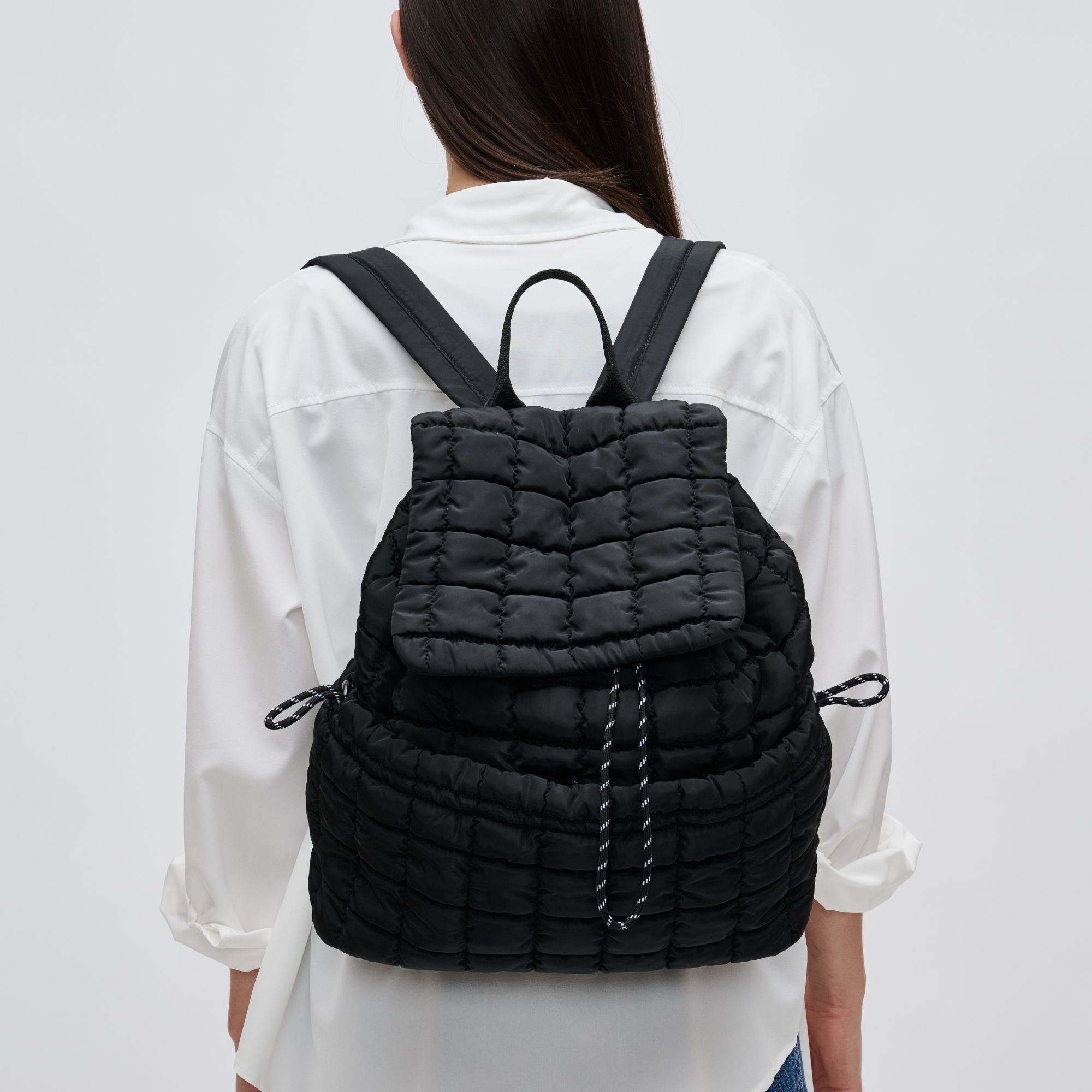 a model in white wearing a black puffer-style backpack