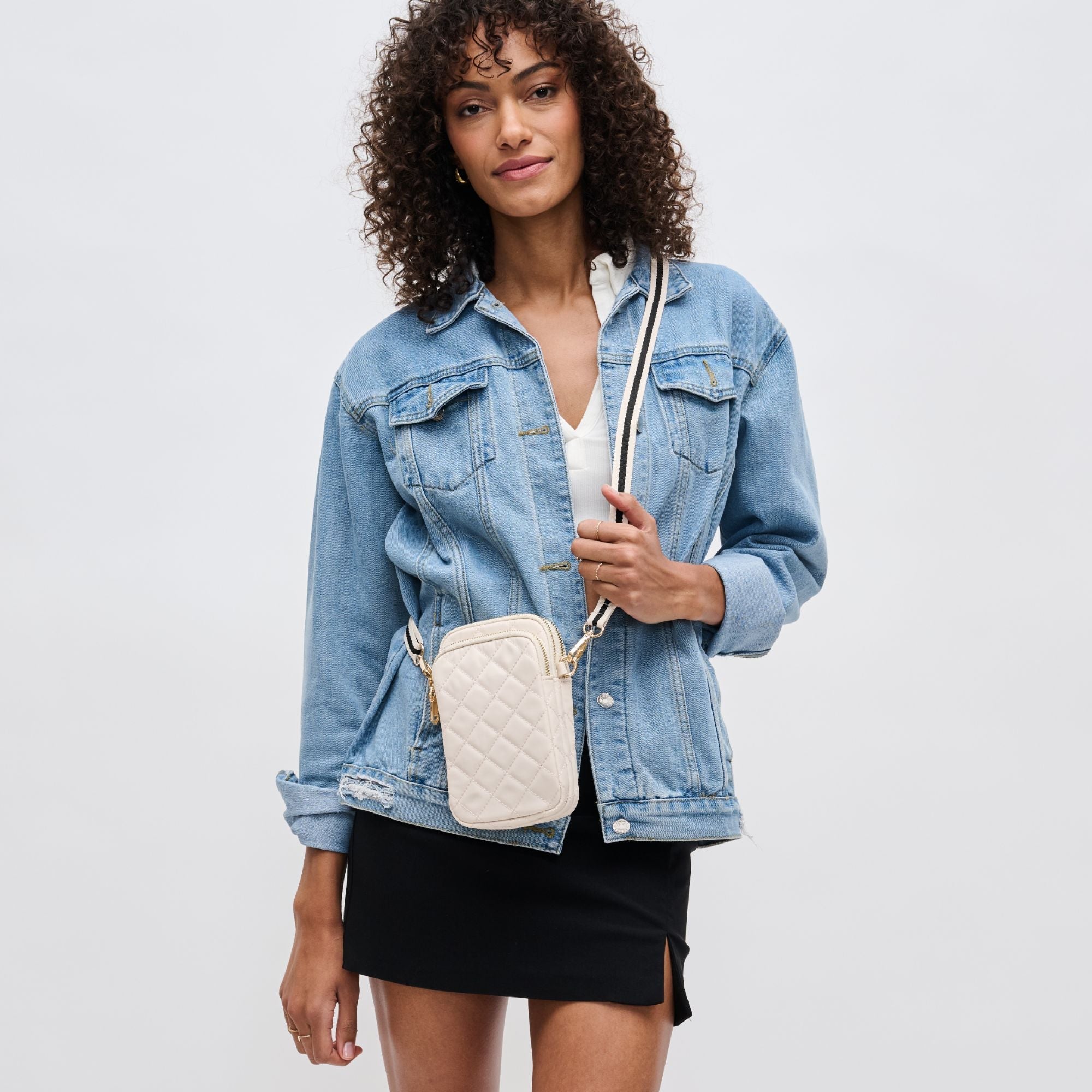 a model in a denim jacket carrying a white crossbody phone bag