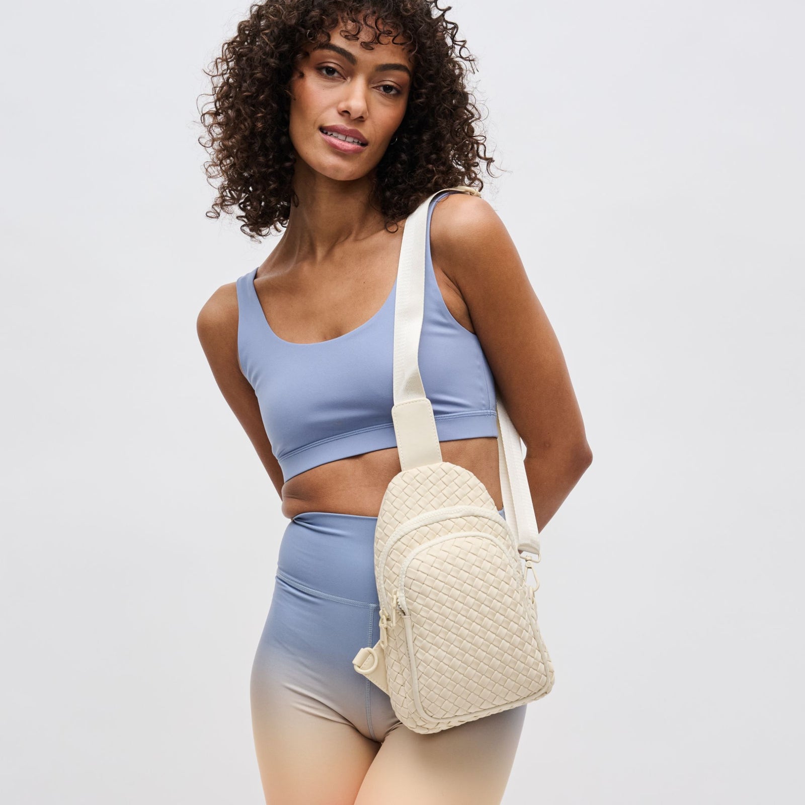 Woman holding a woven cream sling bag